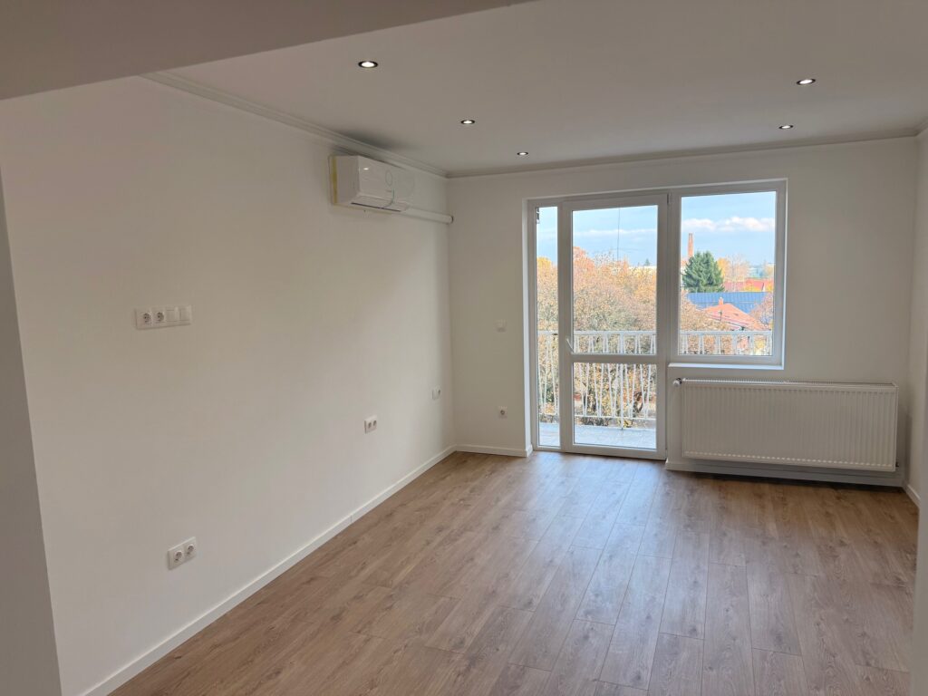 Egy napsütötte nappali, ahol spot lámpák, rejtett hangulatvilágítás és egy klíma van a falon